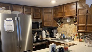 A kitchen with wooden cabinets, stainless steel appliances, and a bar area with stools. - Dog Friendly Condo in White Mountains
Across the Street from StoryLand (Bartlett)