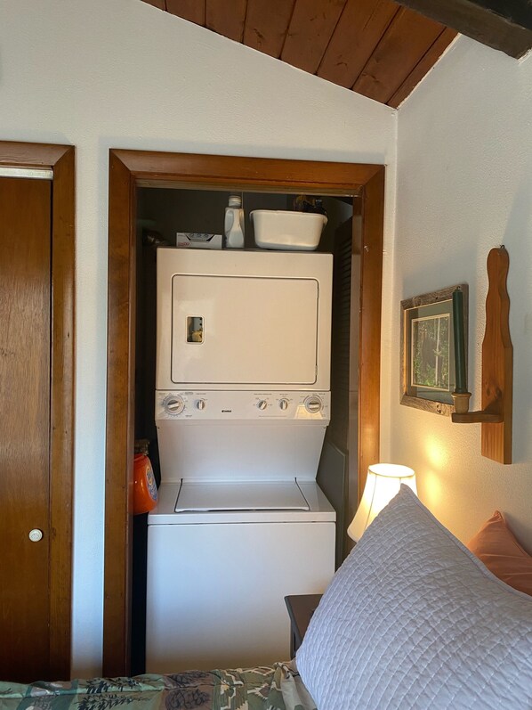 A compact laundry room with a washer and dryer, wooden door frame, and a small table with a lamp.