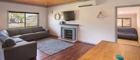 A living room with a grey sofa, a fireplace, a TV mounted above it, and a wooden table.