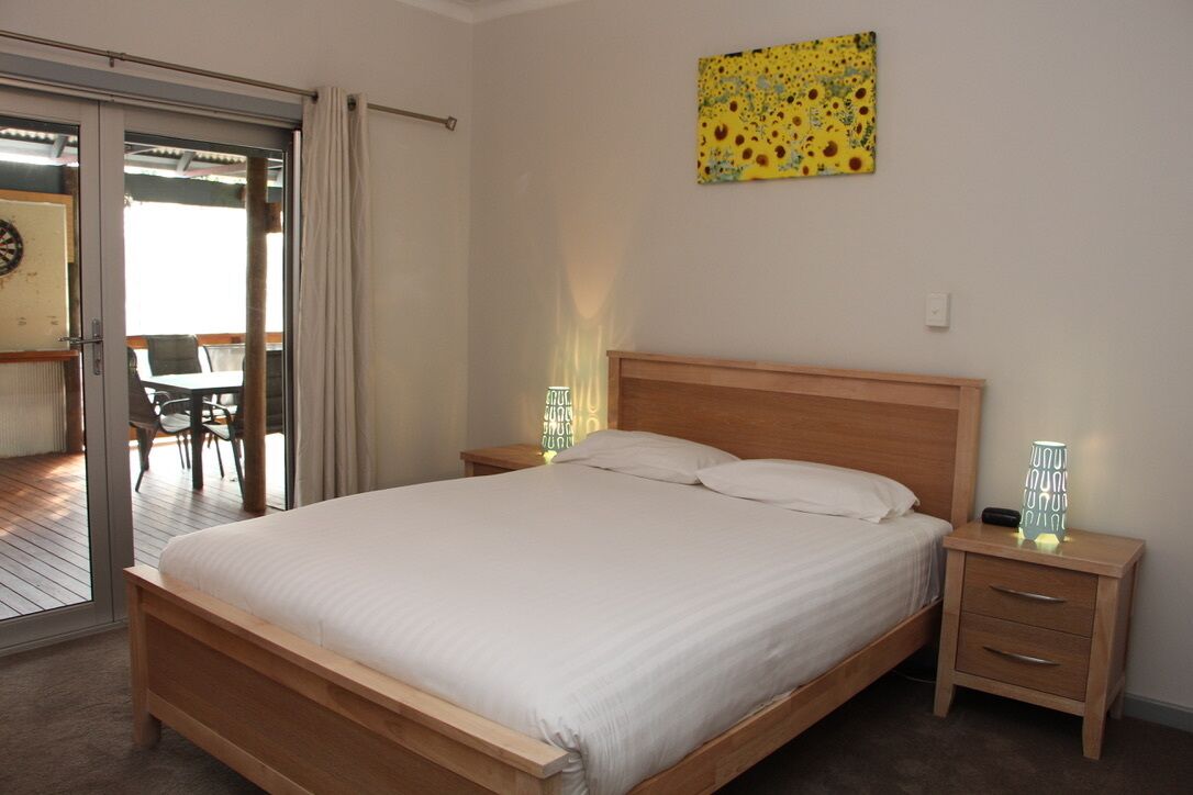 A bedroom with a wooden bed, two bedside tables with lamps, a chair, and a door leading to a balcony.