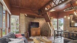 A cozy living room with a stone wall, wooden ceiling, and a television. - Driftaway Cottage - An enchanting escape (Ocean Grove)