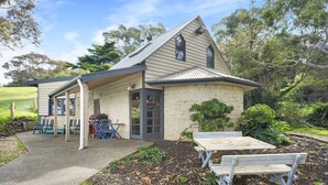 A stone building with a pitched roof, a covered porch, and a small garden area with a picnic table and chairs. - Driftaway Cottage - An enchanting escape (Ocean Grove)