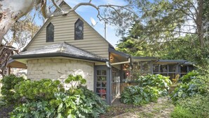 A stone house with a gabled roof, a glass door, and a garden with various plants. - Driftaway Cottage - An enchanting escape (Ocean Grove)