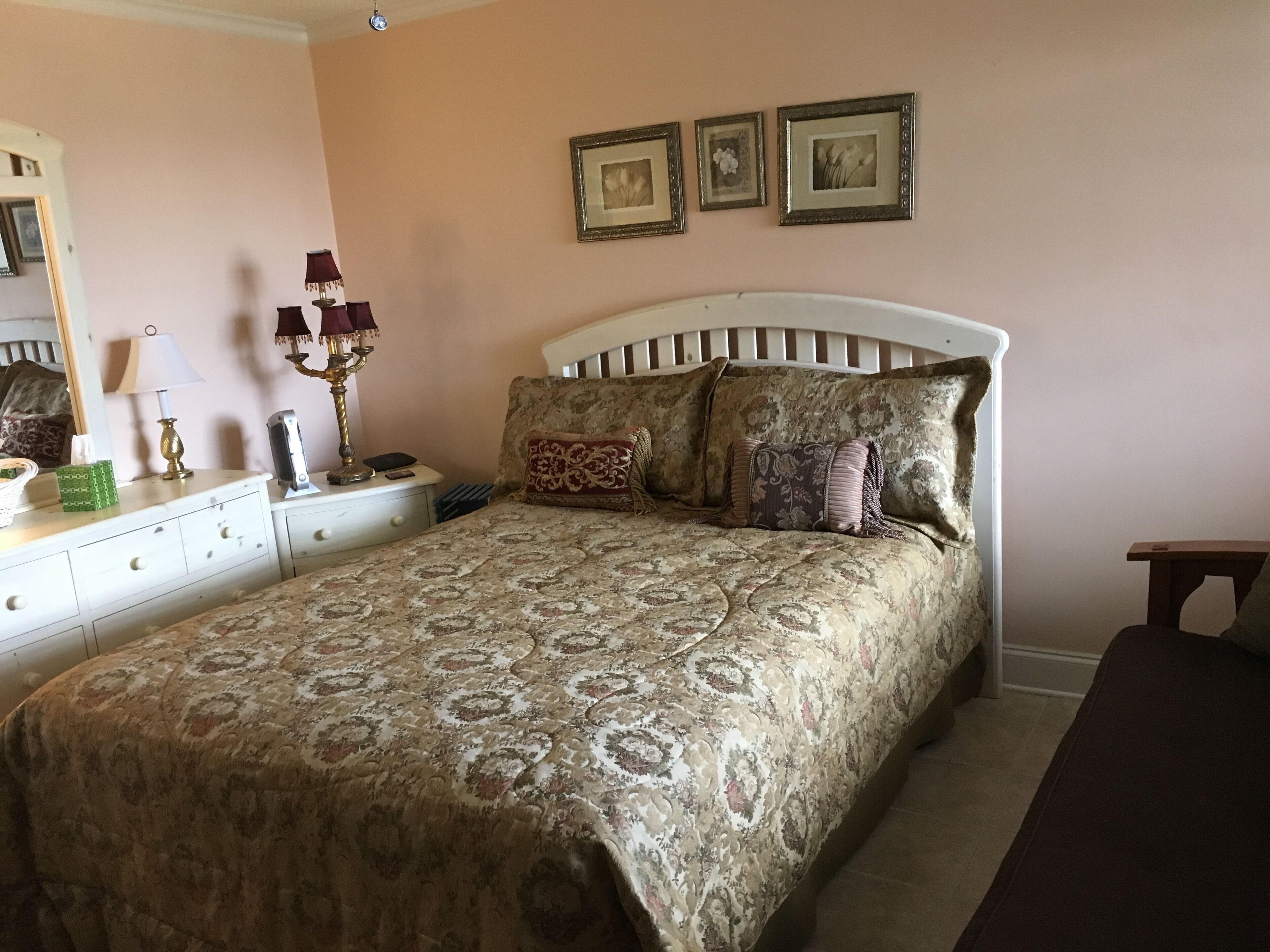 Un dormitorio con cama, mesita de noche, lámpara y cuadros en la pared.