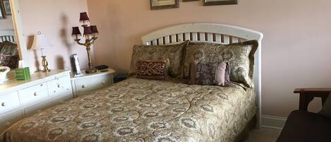 Un dormitorio con cama, mesita de noche, lámpara y cuadros en la pared.