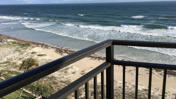 A beach view from a balcony with a railing, ocean waves, and a clear sky. - Awesome 6th Story View Of The Ocean, Pool And Beach  (Ponce Inlet)