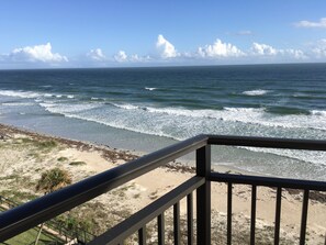 A beach view from a balcony with a railing, ocean waves, and a clear sky. - Awesome 6th Story View Of The Ocean, Pool And Beach  (Ponce Inlet)