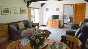 A cozy living room with a brown leather sofa, a wooden dining table with chairs, a television, and a wooden cabinet. - Small, Select Development Of Holiday Cottages (Hartland, Bideford, Devon)