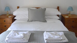 A neatly made bed with a grey quilted pillow, white linens, and two bedside tables with lamps. - Small, Select Development Of Holiday Cottages (Hartland, Bideford, Devon)