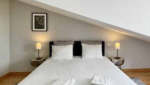 Un lit bien fait, avec du linge de lit blanc et deux serviettes pliées, deux lampes de chevet et un tableau encadré au mur.