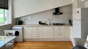 Une cuisine moderne avec des meubles blancs, un lave-linge encastré, une cuisinière à gaz et un four à micro-ondes.