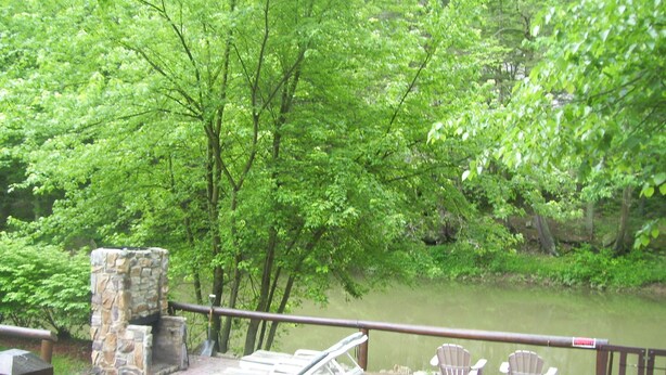 A stone-built deck with lounge chairs and a small table overlooking a pond surrounded by lush greenery.