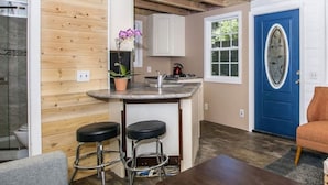 Une cuisine compacte avec un coin bar, des murs en bois, une porte bleue et un seul tabouret.
