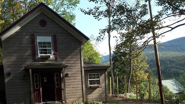 A wooden house with a porch, a small attached structure, and a pathway leading to the house.