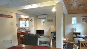 A cozy living room with a dining area, wooden ceiling, and a kitchen in the background.