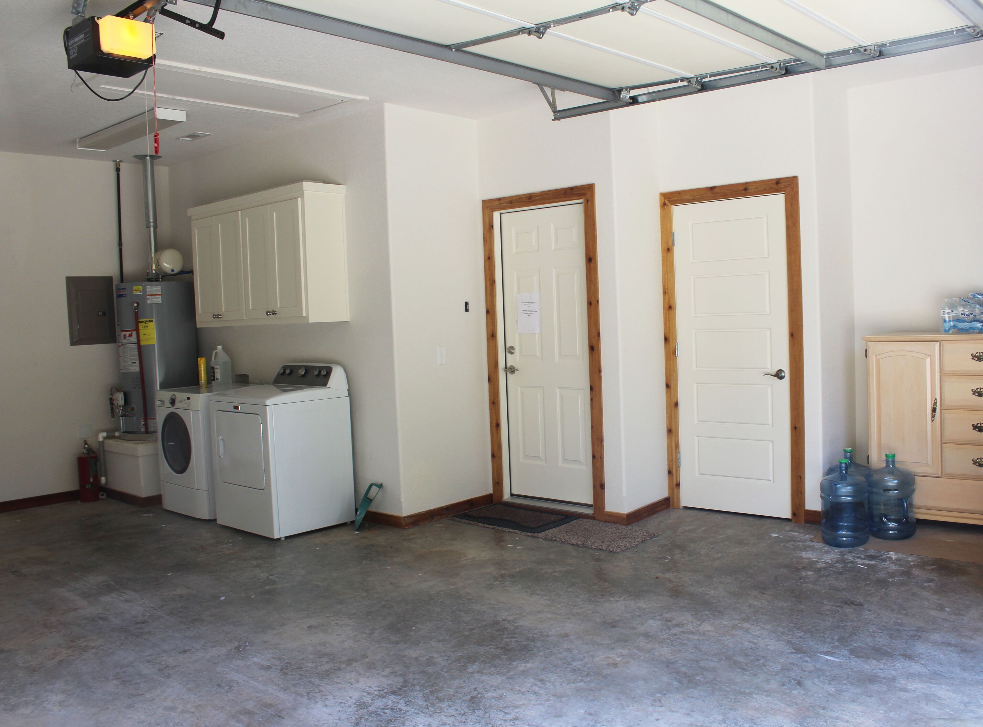 A laundry room with a washing machine, dryer, and cabinets. There are two doors and a water dispenser.