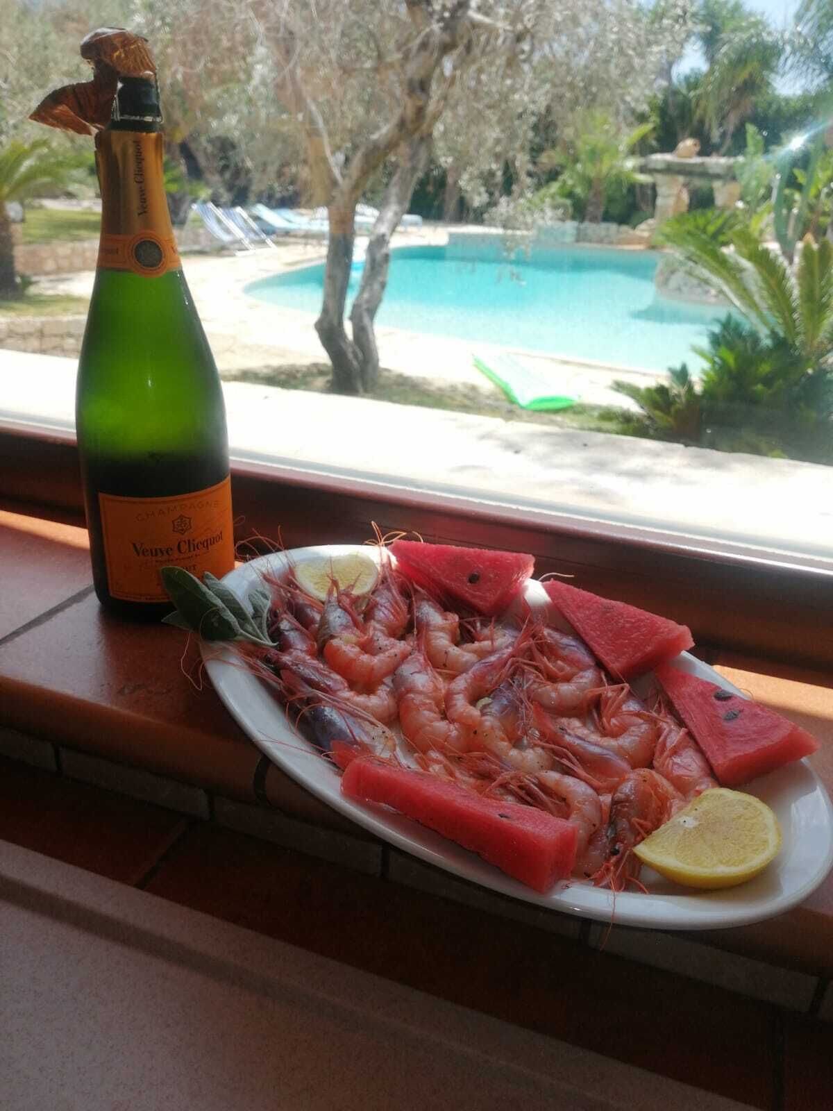 En flaska Veuve Clicquot-champagne och en tallrik med räkor, serverade med vattenmelon och citronskivor, står på en fönsterbräda.