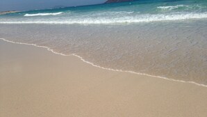 A beach with clear turquoise water, gentle waves, and a distant mountain. - Beachfront Villa with private pool (La Oliva)