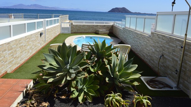 A rooftop pool with a view of the sea and mountains, surrounded by plants and a stone wall. - Beachfront Villa with private pool (La Oliva)