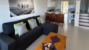A modern living room with a black sectional sofa, a wooden coffee table with decorative items, and a cityscape painting on the wall. - Beachfront Villa with private pool (La Oliva)