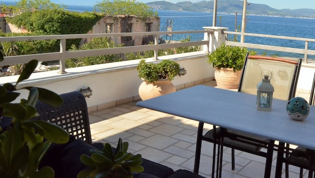 Une terrasse avec une table et des chaises, des plantes en pot et une vue sur la mer.