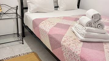 A bed with white pillows, a pink and white quilt, and rolled towels on the side.