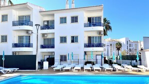 A hotel with a swimming pool, balconies, and lounge chairs.