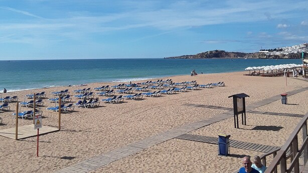 A beach with sun loungers and umbrellas, a lifeguard tower, and a clear view of the sea.