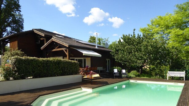 Une terrasse en bois avec une piscine, une maison en bois avec un toit en pente et un banc.
