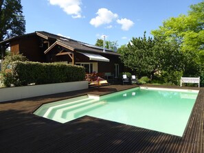 A wooden deck with a swimming pool, a wooden house with a sloped roof, and a bench. - Large 4 Bedroom, 2 bathroom house with large private pool. (Le Buisson-de-Cadouin)