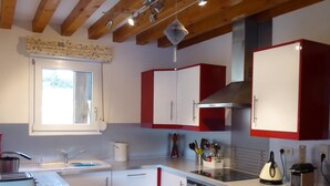 Une cuisine compacte avec des meubles blancs et rouges, un four encastré et une fenêtre au-dessus de l’évier.