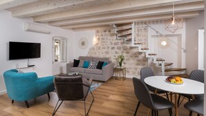 Un salon moderne avec un canapé gris, un fauteuil turquoise et un coin repas comprenant une table blanche et des chaises noires.