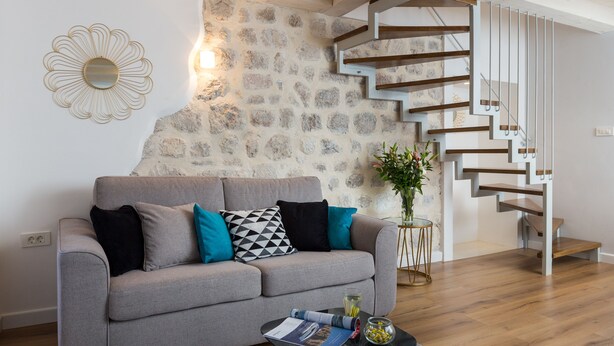 Un salon moderne avec un canapé gris, une table basse avec des magazines, un vase de fleurs et un escalier en bois.