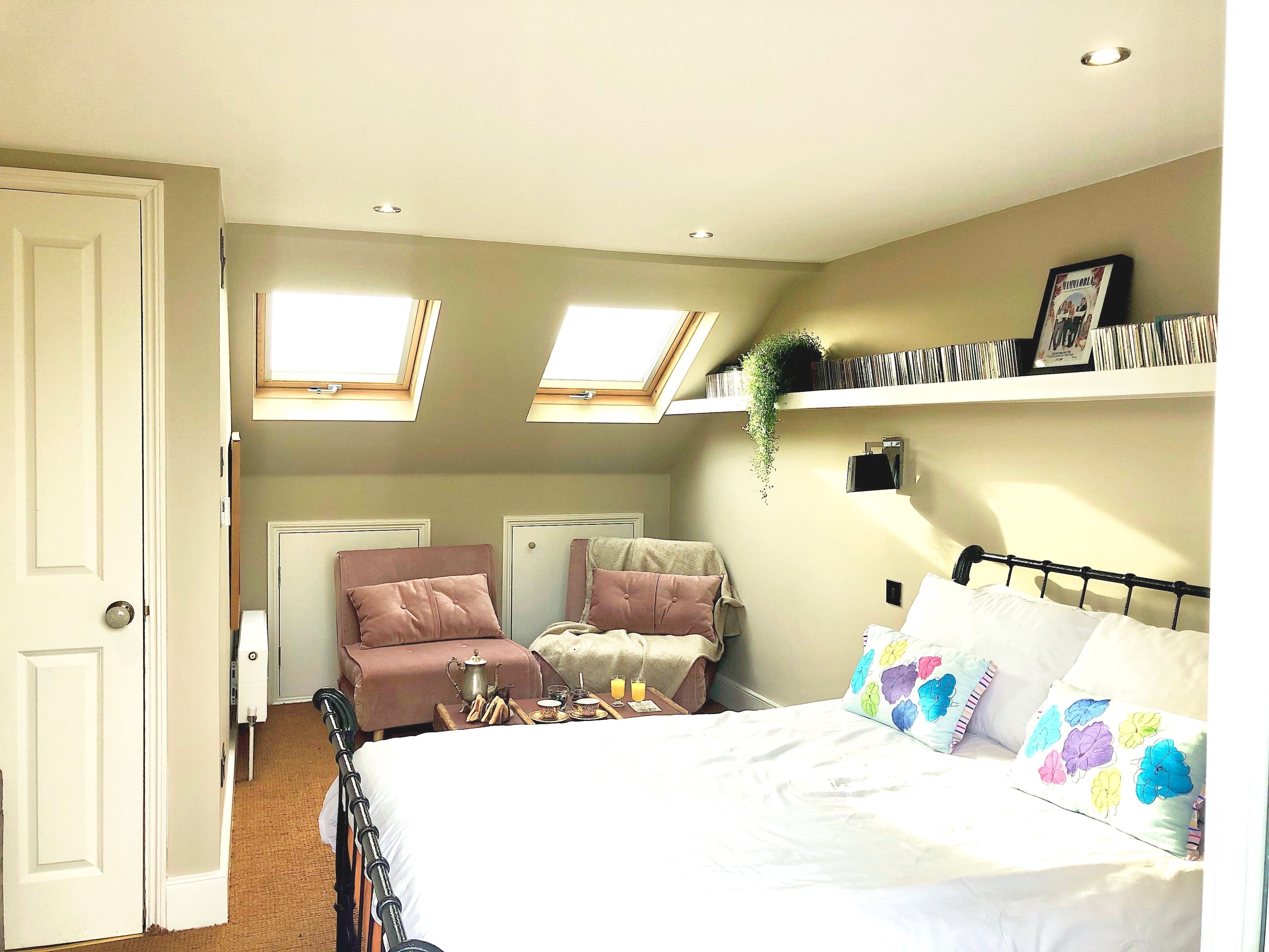 Un dormitorio con cama, una silla, mesita de noche, ventana y estantería con libros.