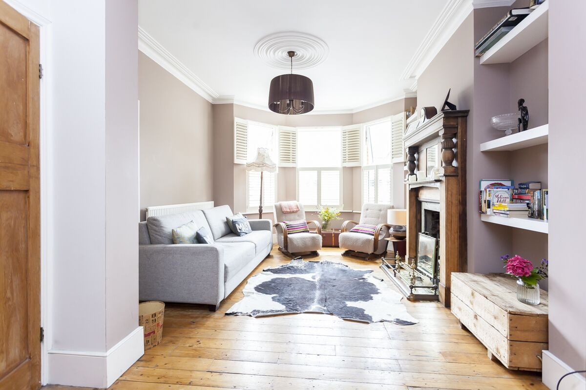 A living room with a grey sofa, two armchairs, a wooden coffee table, and a black and white rug. There is a fireplace with a mirror and a shelf with books and decorative items.
