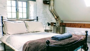 Une chambre à coucher avec un lit, une fenêtre, une lampe et une bouche d’aération au plafond.