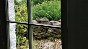 Une fenêtre donnant sur un jardin, avec notamment un mur en pierre et différentes plantes.