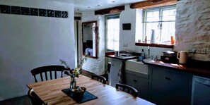 Enjoy a warm meal in this inviting dining area with a table for two, a vase of flowers, and a kitchenette with sink and kettle.