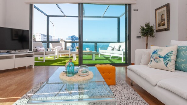 Un salon moderne doté d’une grande porte vitrée donnant sur un balcon avec vue sur la mer.
