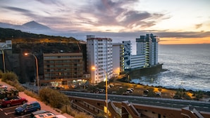 Un paysage urbain côtier avec des immeubles modernes de grande hauteur, une autoroute et une montagne en arrière-plan.