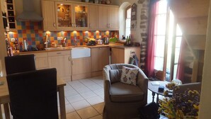 A compact kitchen with wooden cabinets, a tiled backsplash, and a dining area with a chair and table. - Intimate stone-built stable, suitable for couples in a rural setting (Bais)