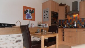 A dining area with a wooden table and chairs, a kitchen with wooden cabinets and a tiled backsplash, and a painting on the wall. - Intimate stone-built stable, suitable for couples in a rural setting (Bais)