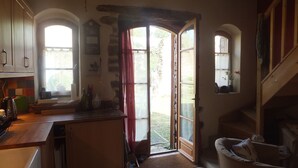 A rustic kitchen with a wooden countertop, a sink, and a window with a view of the garden. There is a door leading to an outdoor area with a stone wall and a red curtain. - Intimate stone-built stable, suitable for couples in a rural setting (Bais)