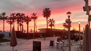 An outdoor seating area with tables and chairs, palm trees, and a sunset in the background. - Luxury 2 Bed Apartment In 5* Villa Sol Village . (Vilamoura)