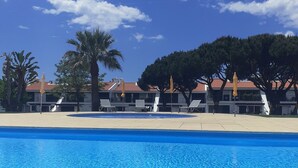 A swimming pool with lounge chairs and umbrellas, surrounded by trees and buildings with red roofs. - Luxury 2 Bed Apartment In 5* Villa Sol Village . (Vilamoura)