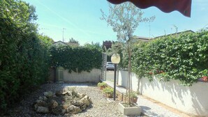 A courtyard with a gravel path, potted plants, a small tree, and a wall with climbing plants.