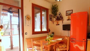 A compact kitchen with a wooden table, chairs, a red refrigerator, and a window with wooden shutters.