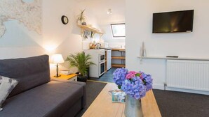 A modern living room with a sofa, a coffee table with flowers, a TV, and a kitchen in the background.