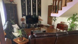 Een woonkamer met een bruine leren bank, een glazen salontafel, een televisie en potplanten.