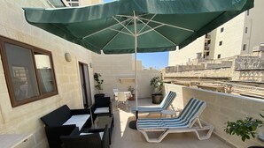 Una terraza en la azotea con zona de comedor, sillones de descanso y plantas en macetas.